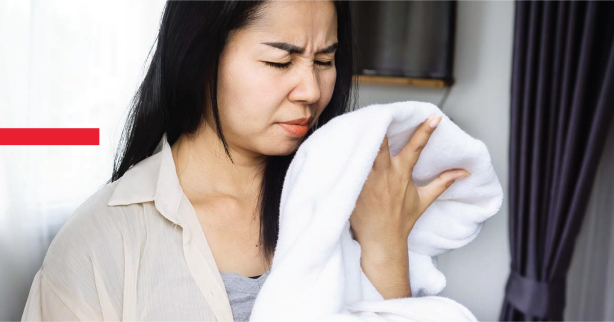 PrestigeBlog RiskofDryerVentFire 03 ✦ Prestige Duct Cleaning Woman Holding And Smelling Damp, Musty Laundry Out Of Her Dryer - A Key Warning Sign Of A Dryer Vent Fire